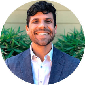 image of Caue wearing a white dress shirt and blue blazer smiling at the camera