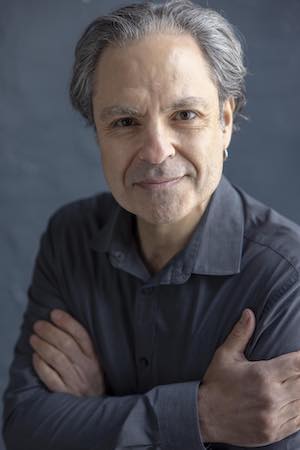 image of David leaning forward with his arms crossed, wearing a blue ling sleeve shirt, half smiling at the camera