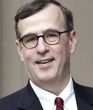 image of Frank wearing glasses and a suit smiling at the camera