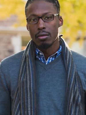 headshot of John wearing glasses in a blue swetaer and striped scarf