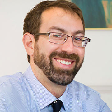 image of Samuel wearing a blue dress shirt and glasses, amiling at the camera
