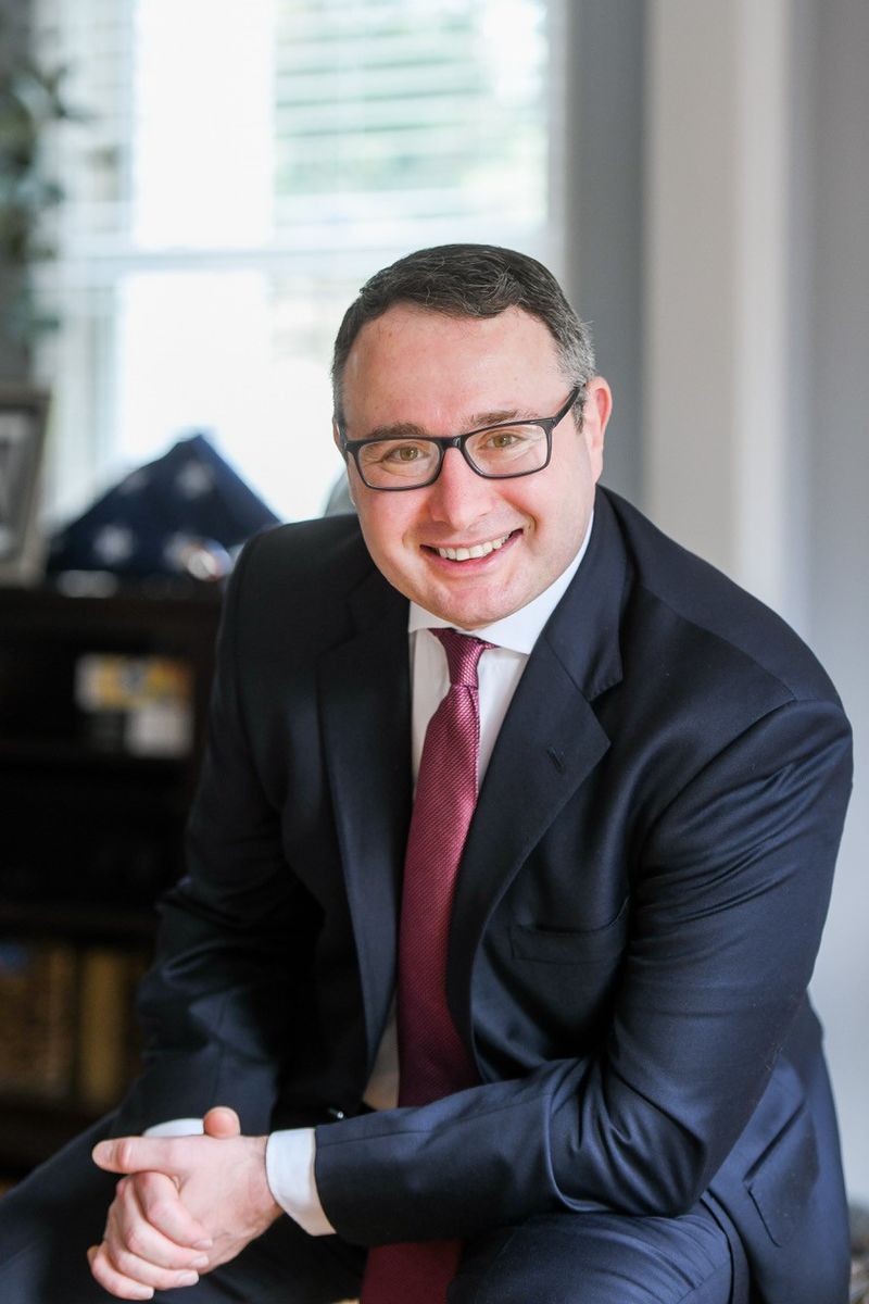 image of Alexander Vindman wearing glasses, in a black blaze, white button down shirt and red tie