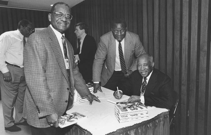Temple Times Photographs. Bernard C. Watson's book signing, February 21, 1997. L-R [standing] James S. White and Charles L. Blockson; [seated] Bernard C. Watson