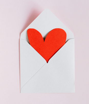 A red heart peeking out of a white envelope
