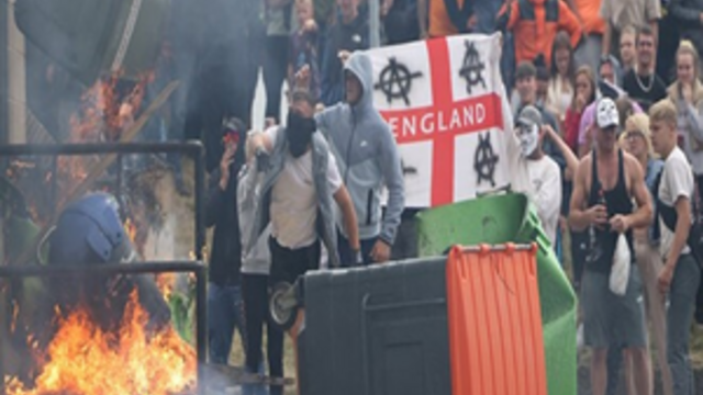 image of protesters in England standing in a group setting a trash can on fire