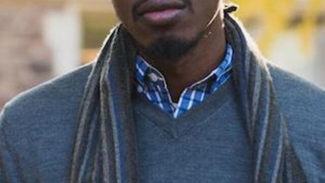 headshot of John wearing glasses in a blue swetaer and striped scarf