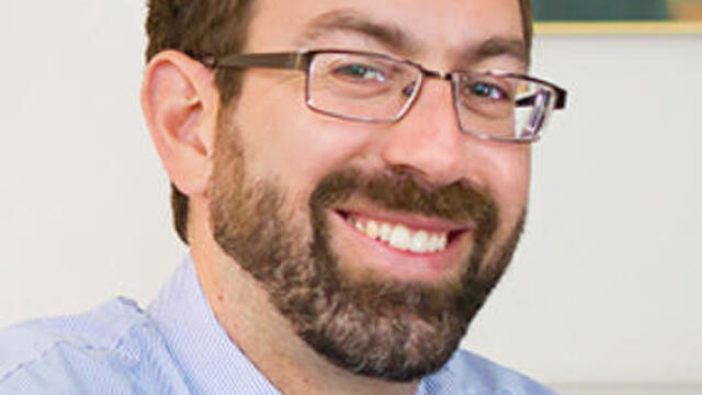 image of Samuel wearing a blue dress shirt and glasses, amiling at the camera
