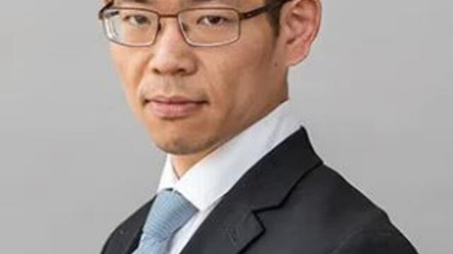 image of Ohyun wearing a blue suit and tie and glasses looking at the camera