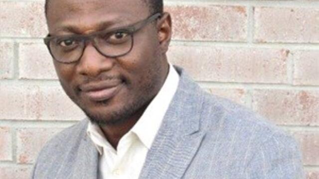 image of Oluwayomi wearing glasses, a grey suit, short cut hair looking at the camera