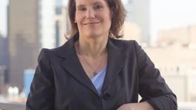image of Teresa standing with the city in the background wearing a grey suit and blue top with her arms crossed