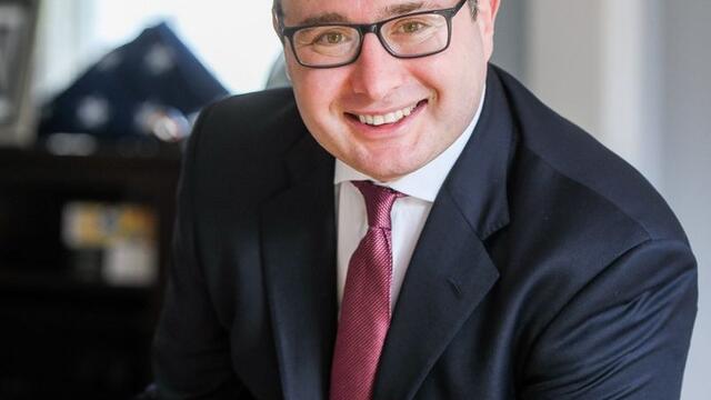 image of Alexander Vindman wearing glasses, in a black blaze, white button down shirt and red tie