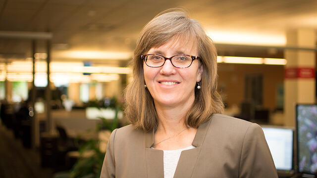 A woman wearing glasses and a brown blazer.