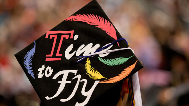 A Temple graduate triumphantly raising his cap at commencement.