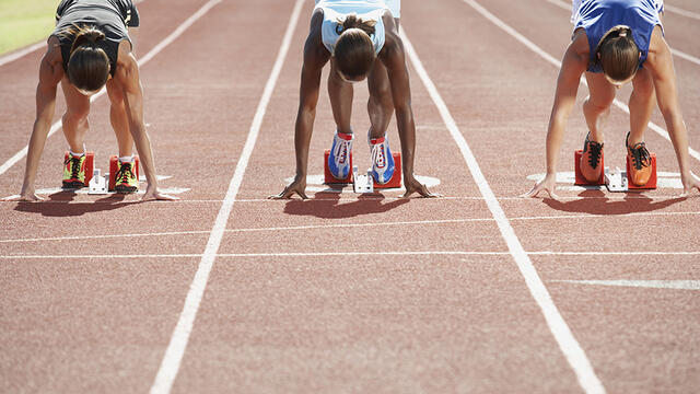 Women runners kneeling on the track before a race starts.