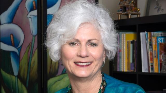 Lisa Kay wearing a teal jacket and standing in front of a bookcase.