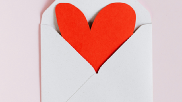 A red heart peeking out of a white envelope