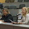 Two women sitting at a table and one is speaking into a microphone.