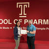 Faculty co-advisors in front of a red wall with the Temple T and the award